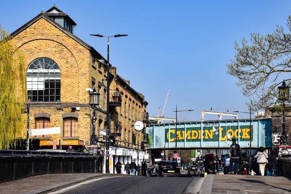 A bustling outdoor market scene in Bethnal Green with numerous vendors displaying clothing and accessories on metal racks and tables, set against a backdrop of modern high-rise buildings under constru