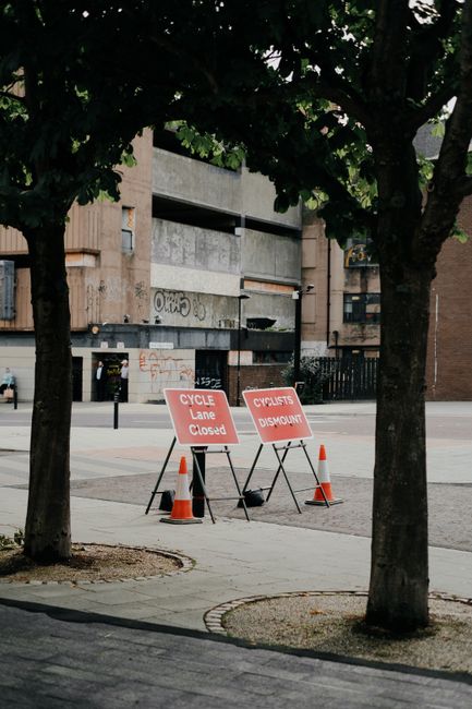 A street scene in Bethnal Green showing a metal signpost with a blue cycling lane sign indicating shared bicycle and pedestrian use, positioned above a yellow warning sign that states 'Road Closed Thi